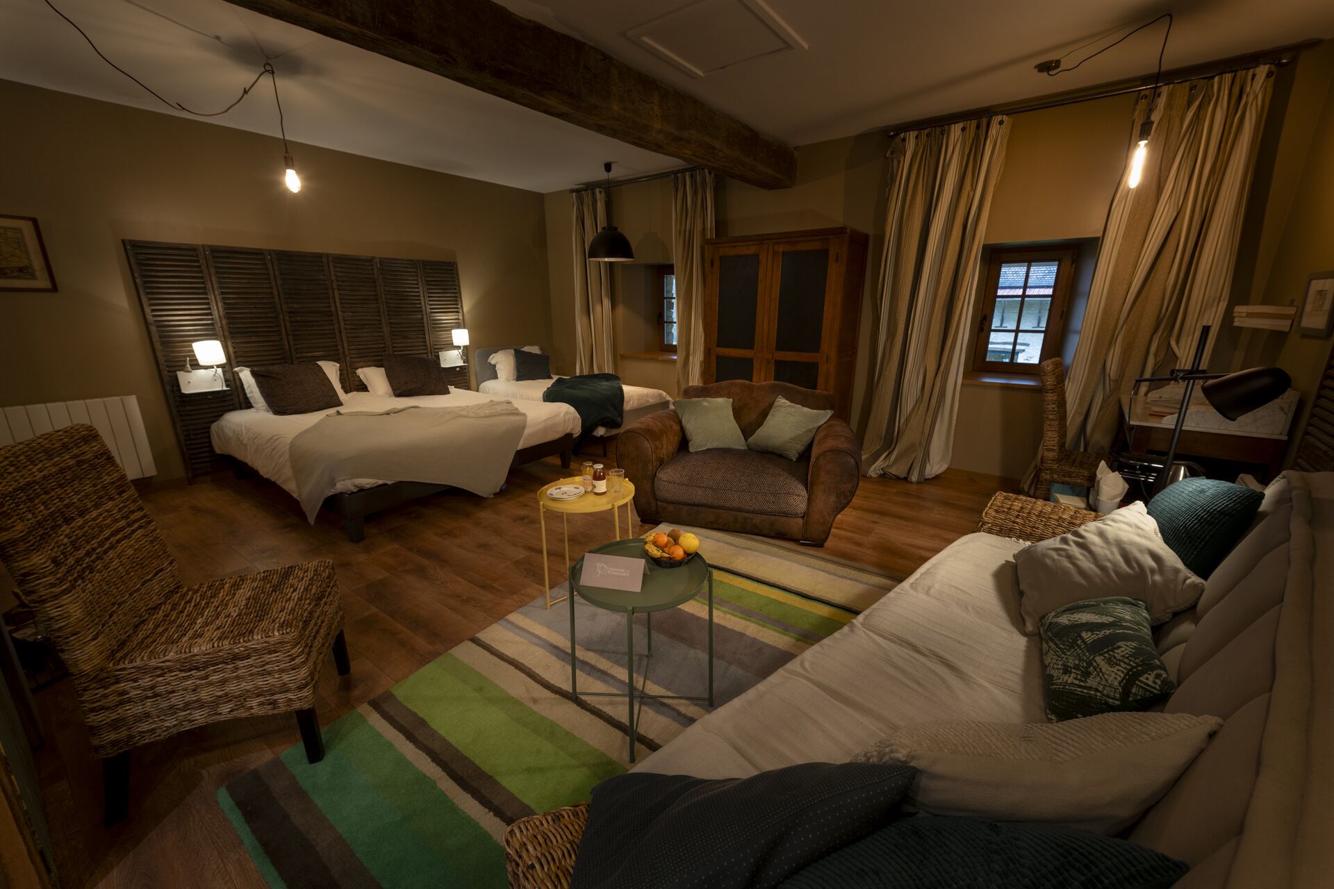 A cozy hotel room with two beds, a sofa, a chair, and a small table with fruit.