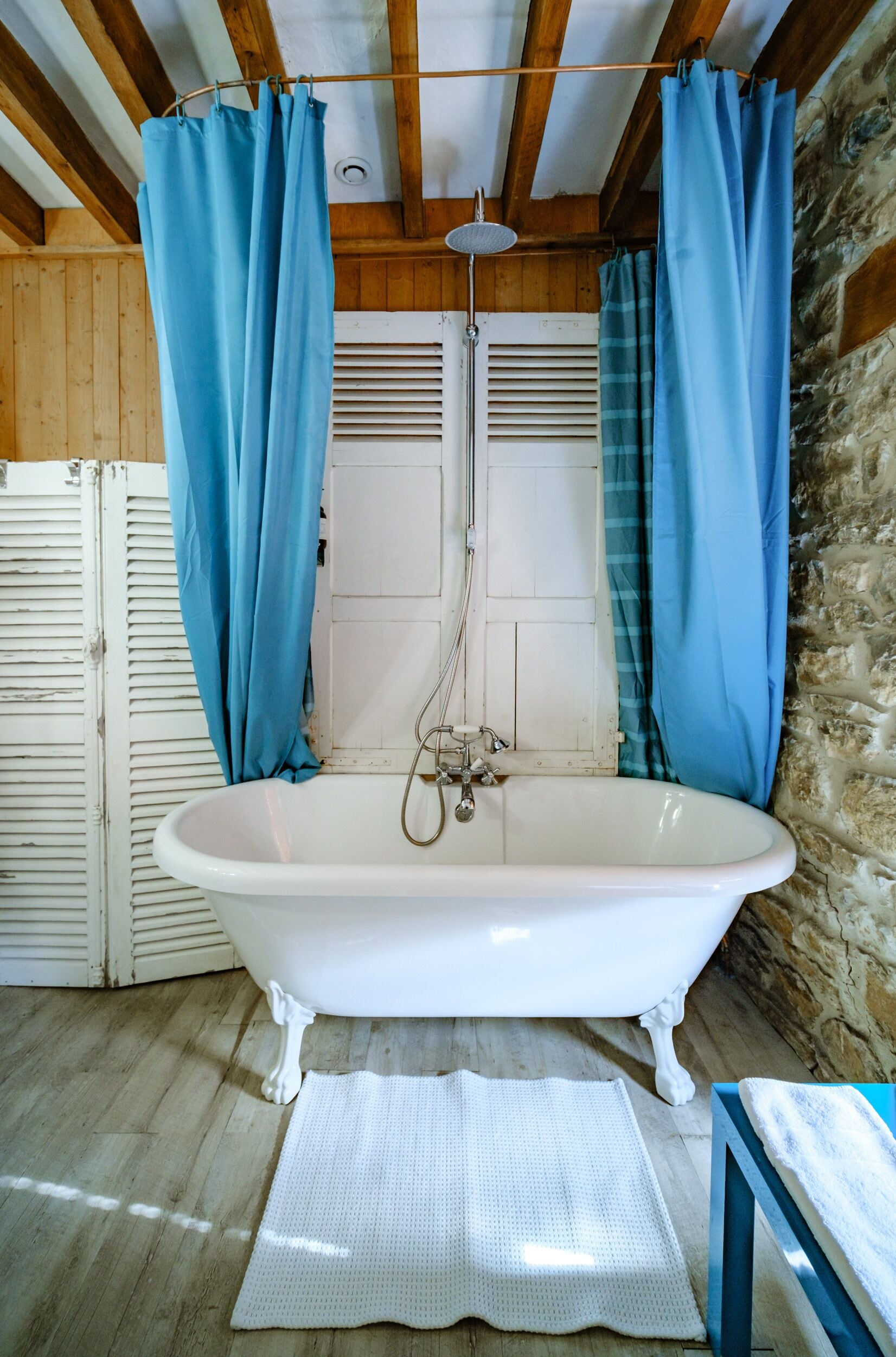 Une salle de bain avec une baignoire sur pieds blanche, des rideaux bleus et un mur en pierre.