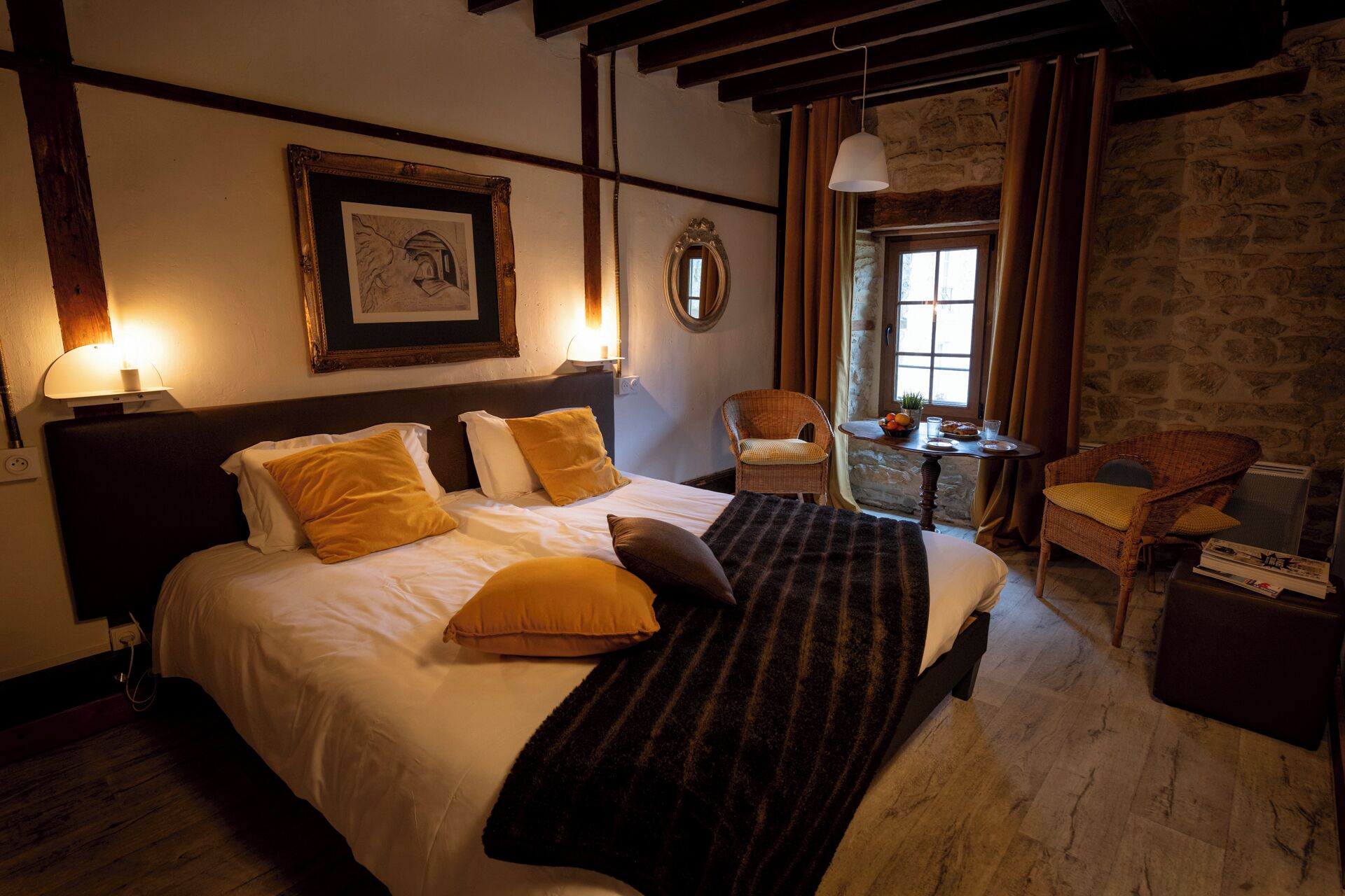 Habitación de hotel con una cama grande, dos sillas, una pequeña mesa con alimentos para el desayuno, un espejo y un cuadro en la pared.