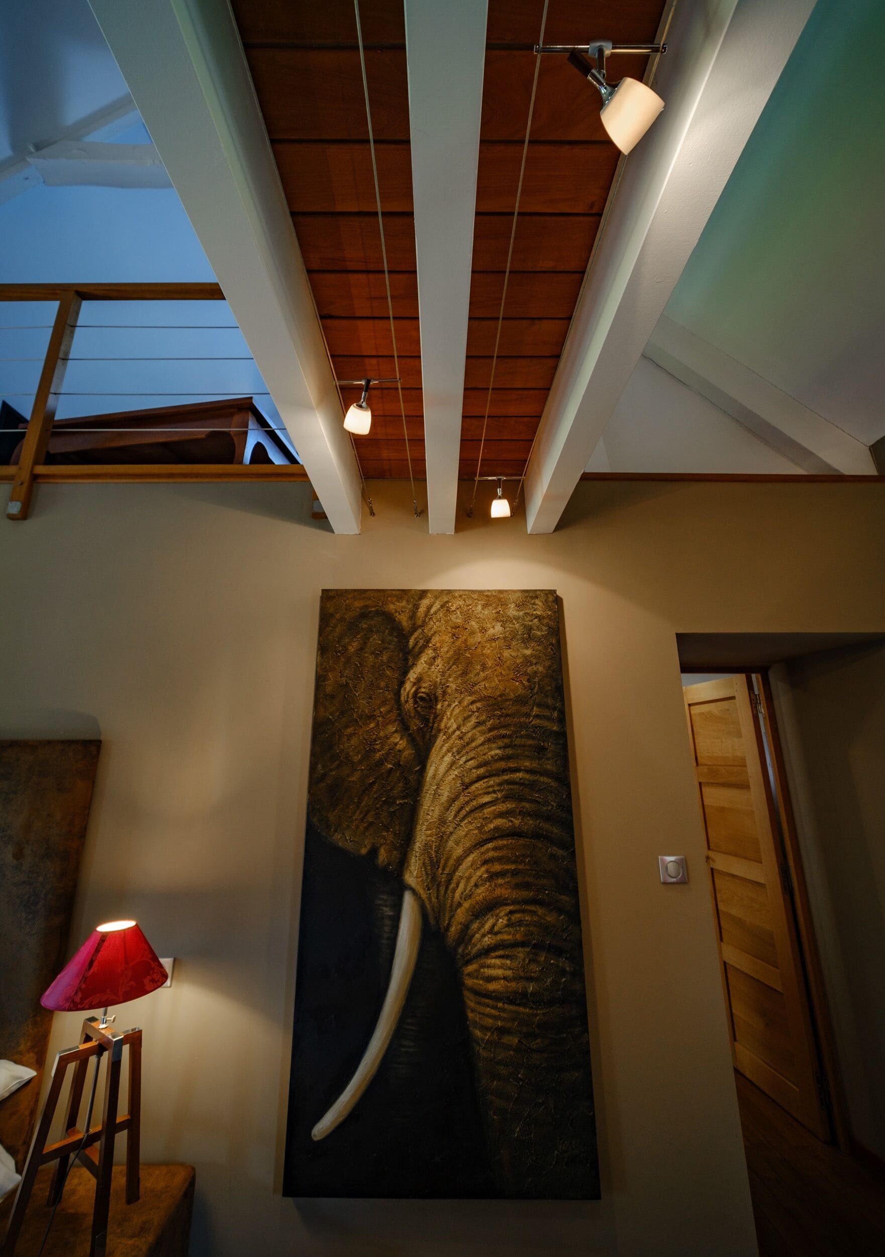 A room with a large elephant painting on the wall, a red lamp, and a wooden ceiling structure.