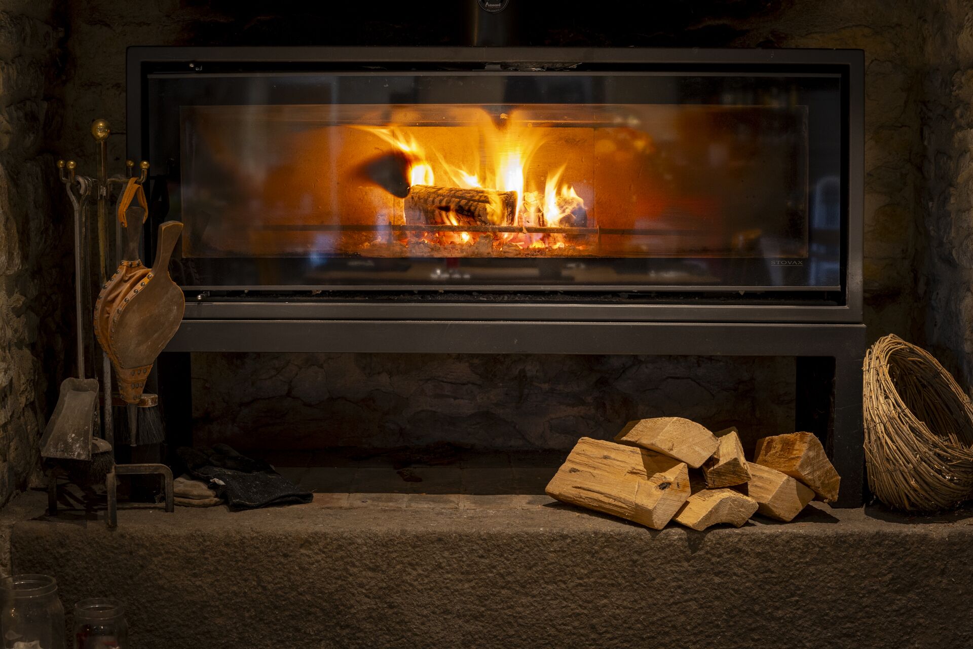 A modern fireplace with a glass front, logs, and a stone wall.