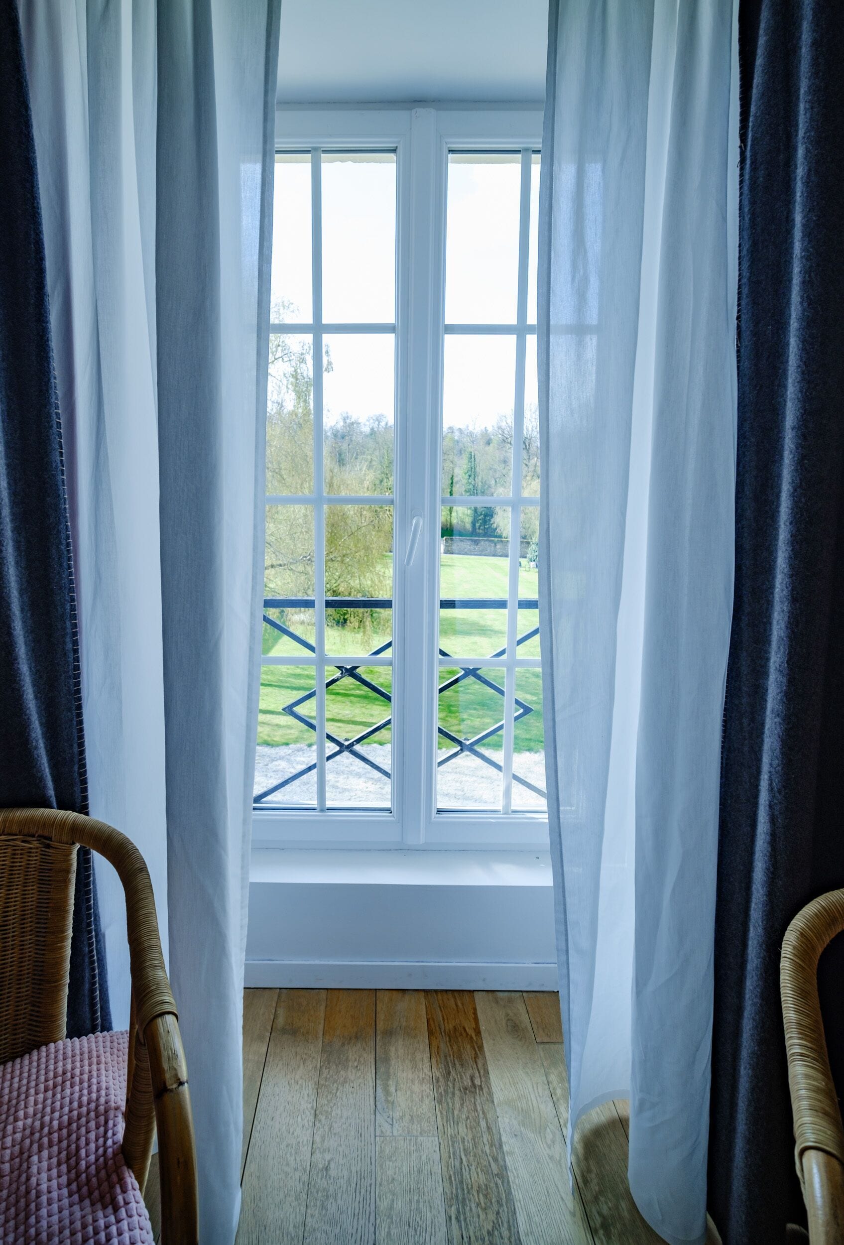 A room with a large window, wicker chairs, and a wooden floor.