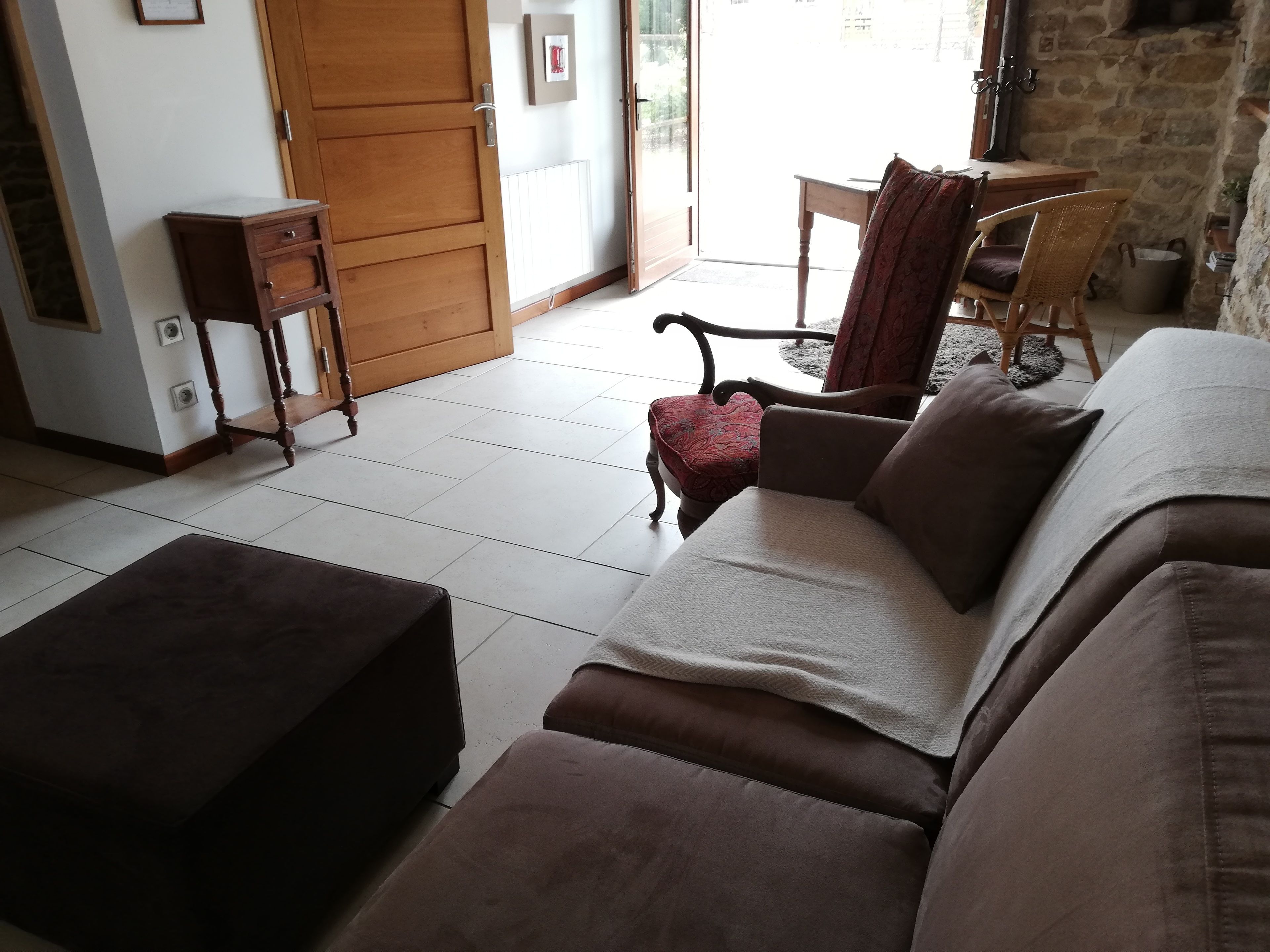 A living room with a brown sofa, a wooden side table, and a chair. There is a door leading to an outdoor area.