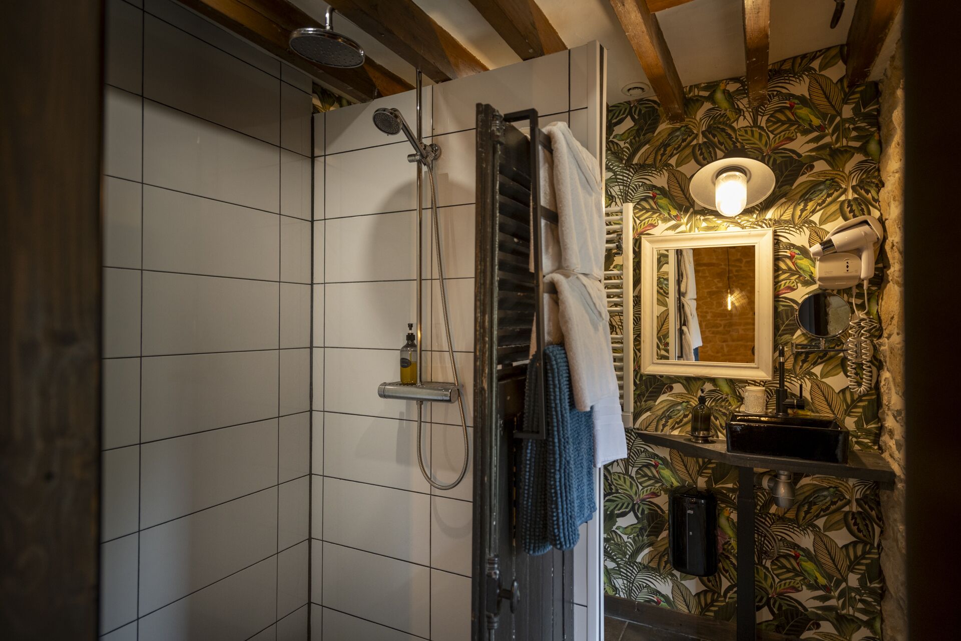 Un bany amb dutxa, parets revestides de rajoles, un mirall i un lavabo amb portaToalles.
