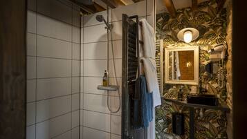 Un bany amb dutxa, parets revestides de rajoles, un mirall i un lavabo amb portaToalles.