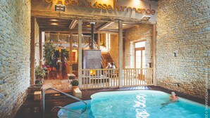 An indoor swimming pool area with a stone wall, wooden deck, and a sign reading "SpaDeltaSuisseNormandie". - Au Domaine de la Pommeraye & Spa (La Pommeraye)