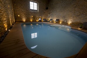 An indoor swimming pool with stone walls and wooden deck. - Au Domaine de la Pommeraye & Spa (La Pommeraye)