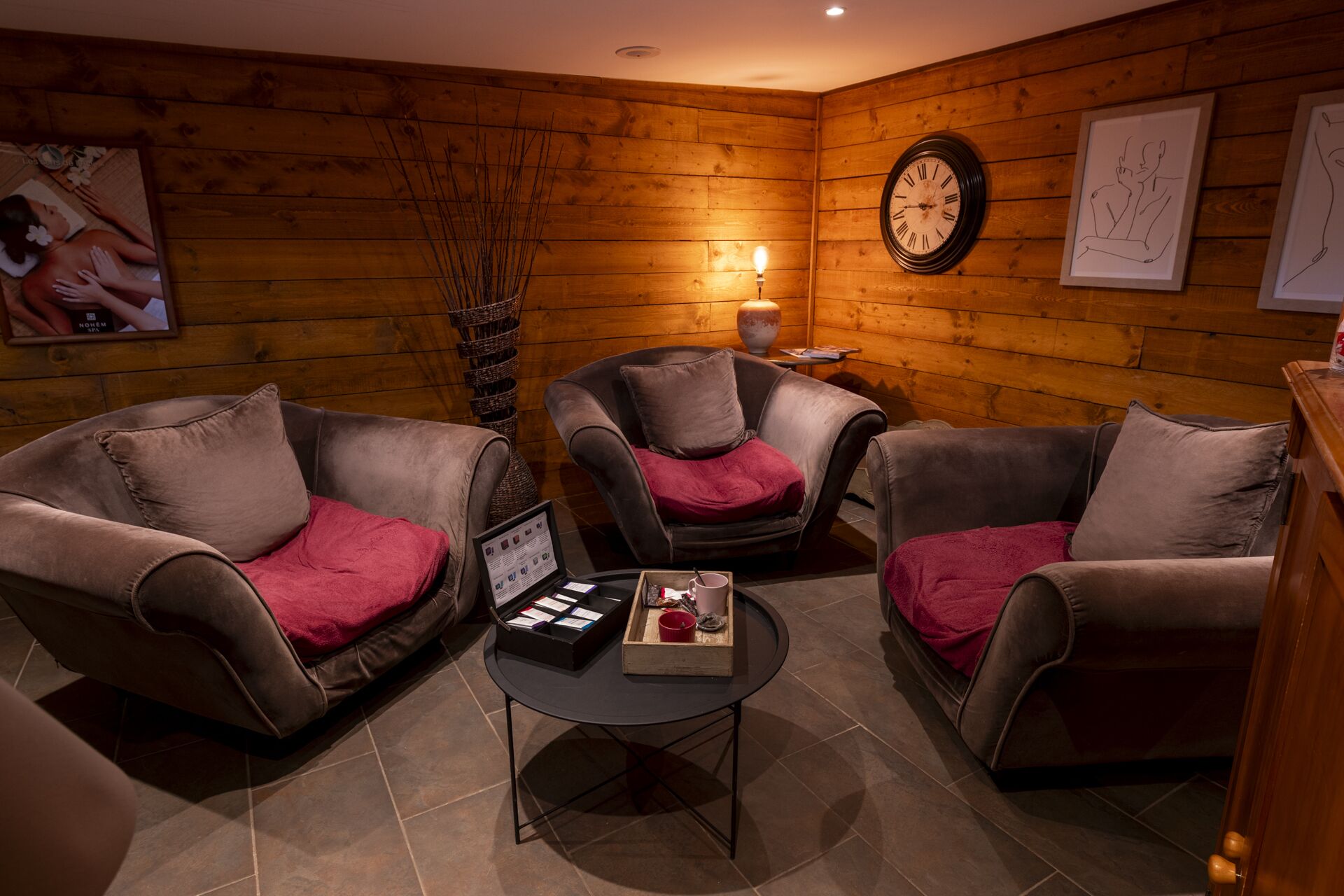 Una habitación acogedora con paredes de madera, dos sillones con cojines rojos, una mesa redonda con una bandeja de objetos, un reloj de pared y obras de arte enmarcadas.