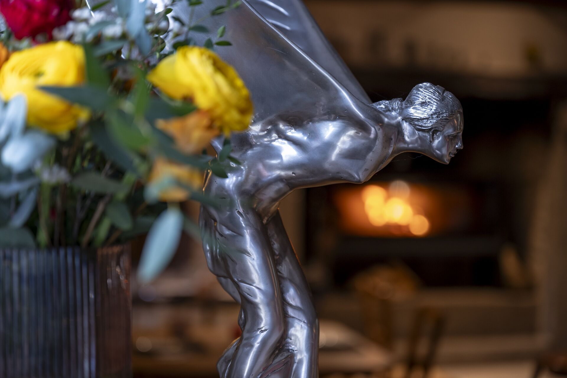 En skulptur af en menneskelig figur i en bøjning, placeret i en vase med gule og røde blomster.