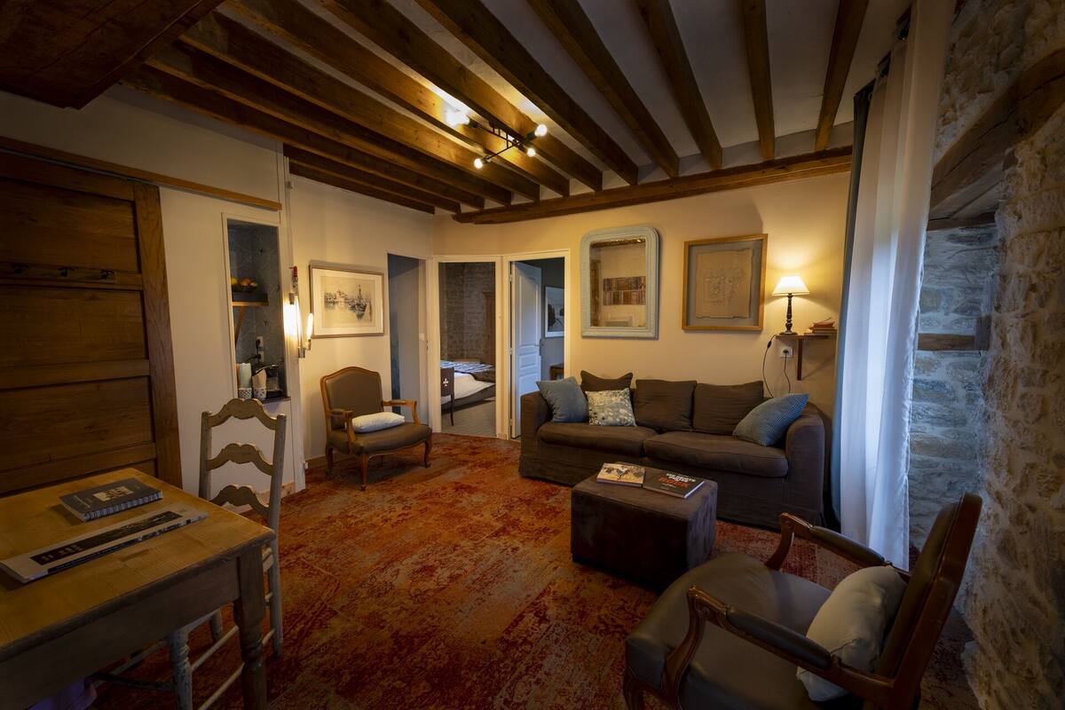 A cozy living room with a wooden ceiling, a sofa, a chair, a small table, and a bookshelf.