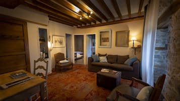 A cozy living room with a wooden ceiling, a sofa, a chair, a small table, and a bookshelf.