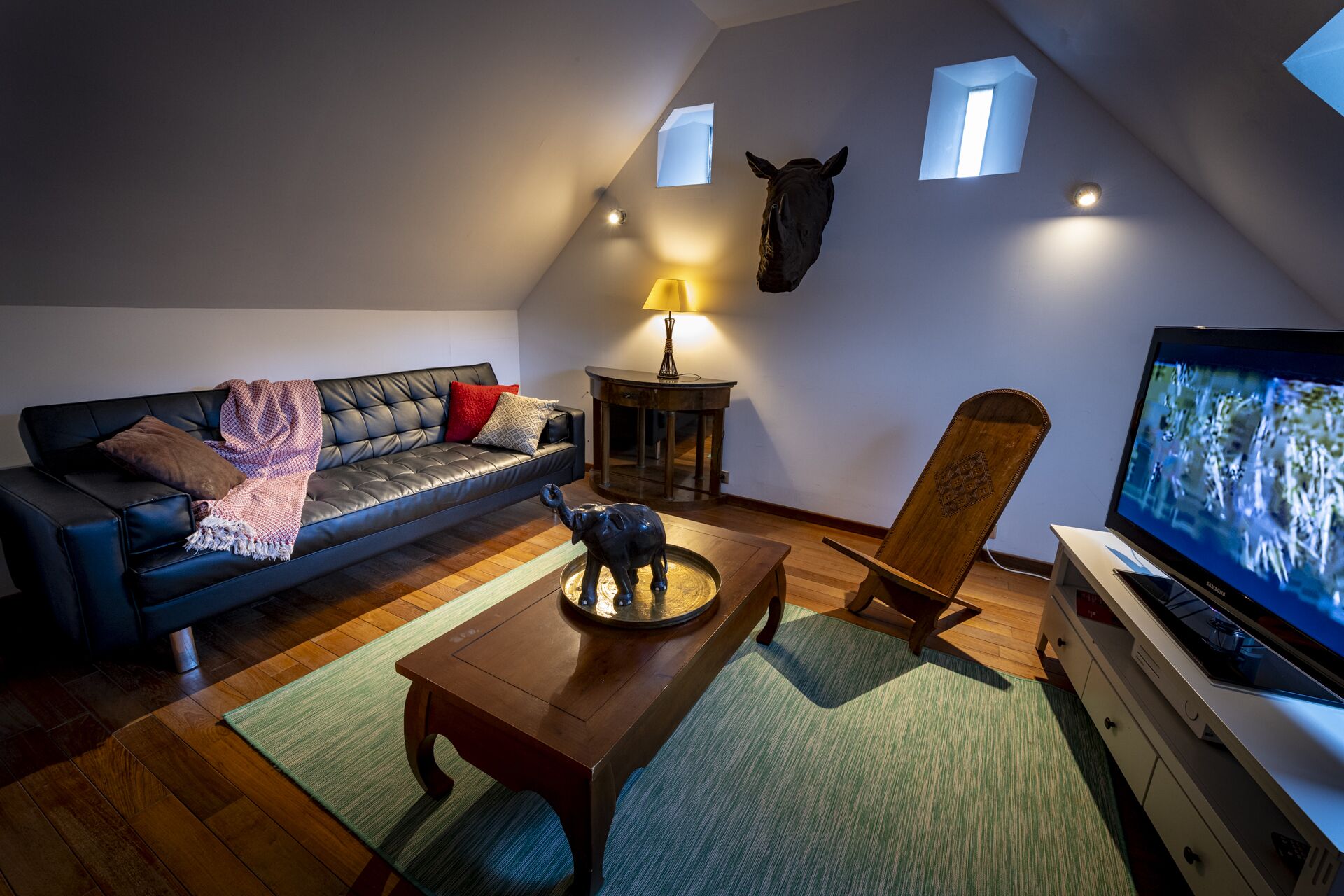 A cozy loft-style living room with a black leather sofa, a wooden coffee table, a TV, and a small statue.