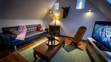 A cozy loft-style living room with a black leather sofa, a wooden coffee table, a TV, and a small statue.