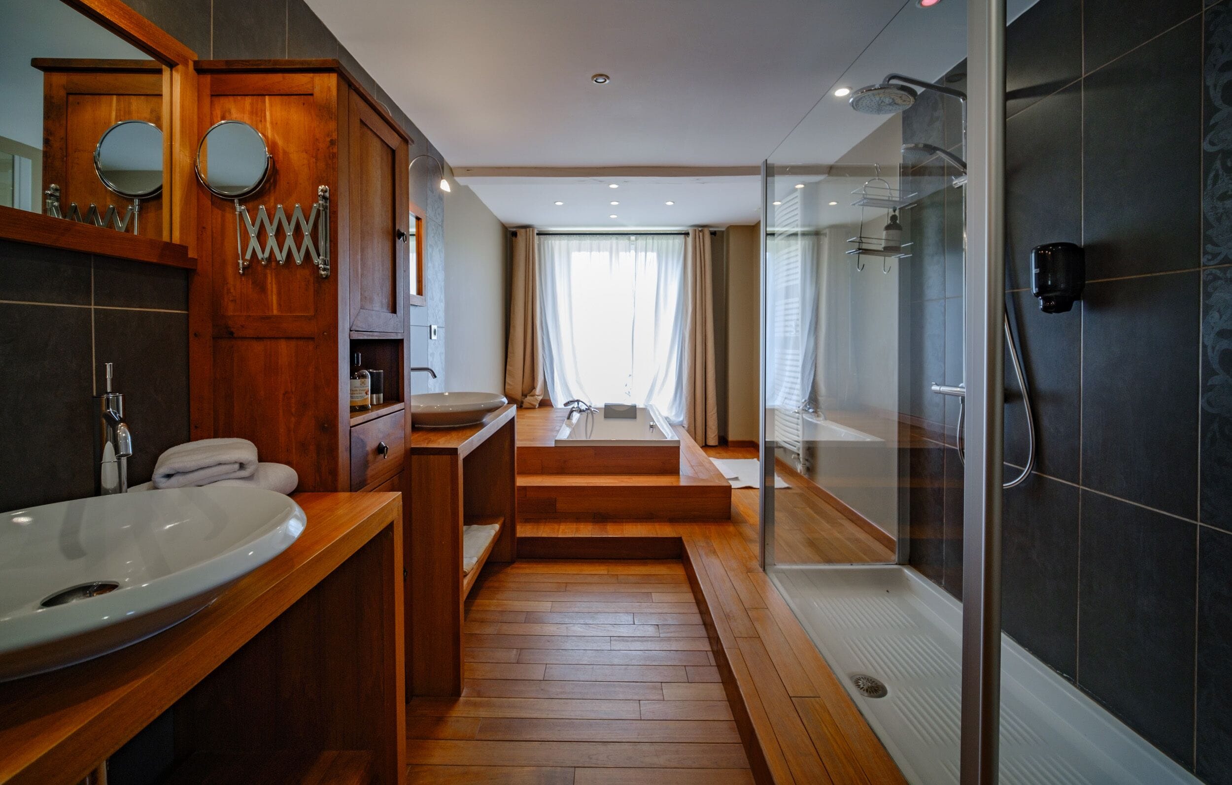 Un baño moderno con tocador de madera, un lavabo amplio, una bañera y una zona de ducha con cerramiento de vidrio.
