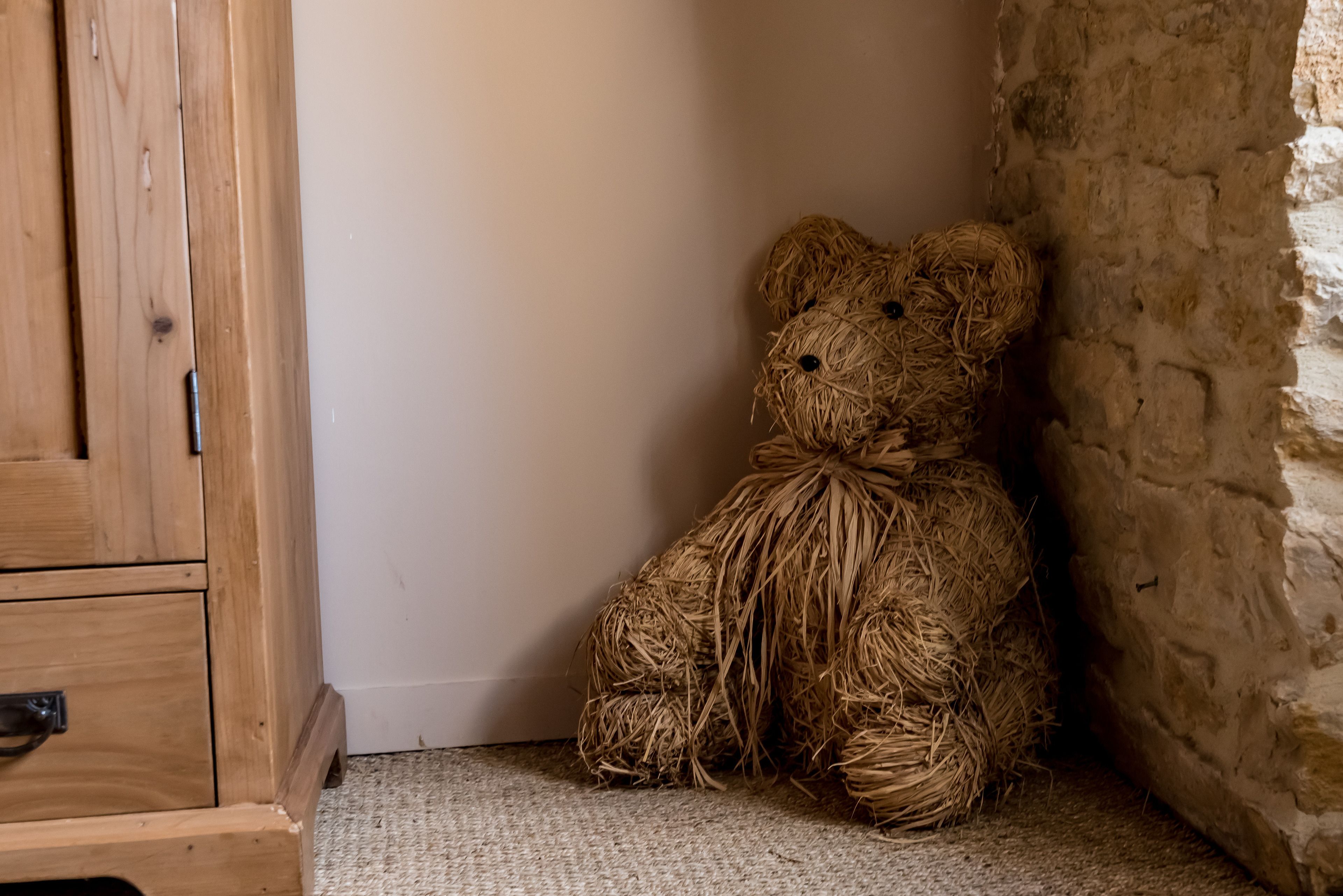 A rustic wooden cabinet and a straw bear decoration in a corner with a textured floor.