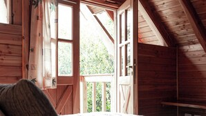 A wooden cabin room with a bed, a ceiling fan, and a view of the outdoors. - Cocos Cura Casas de Montaña (San Carlos de Bariloche)