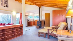 A cozy living area with a fireplace, wooden furniture, and a kitchen in the background. - Cocos Cura Casas de Montaña (San Carlos de Bariloche)