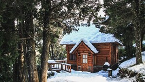 A wooden cabin surrounded by trees with a snow-covered roof and a wooden deck. - Cocos Cura Casas de Montaña (San Carlos de Bariloche)