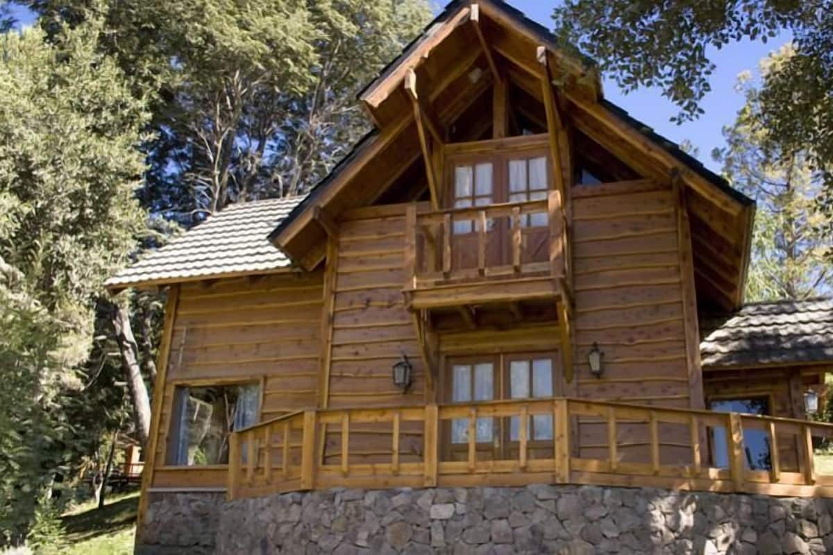 Une cabane en bois avec des fondations en pierre, un balcon et un petit porche.