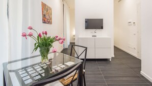 A modern dining area with a glass table, chairs, and a vase of pink tulips. A flat-screen TV is mounted on the wall above a white cabinet. - Residenza Ottaviano 105 by Hili (Rome)