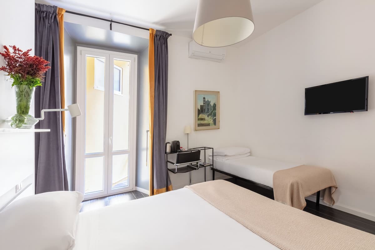 A hotel room with a bed, a desk, a chair, a TV, and a window with curtains.