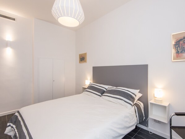 Un dormitorio moderno con cama, lámparas de noche, cabecera y un cuadro en la pared.