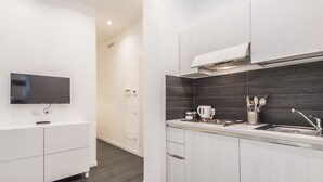 A modern kitchen with a flat-screen TV, white cabinets, dark backsplash, and a stainless steel sink. - Residenza Ottaviano 105 by Hili (Rome)