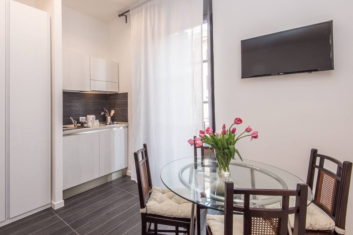 A modern kitchen with white cabinets, a black backsplash, and a dining area with a glass table and wooden chairs.