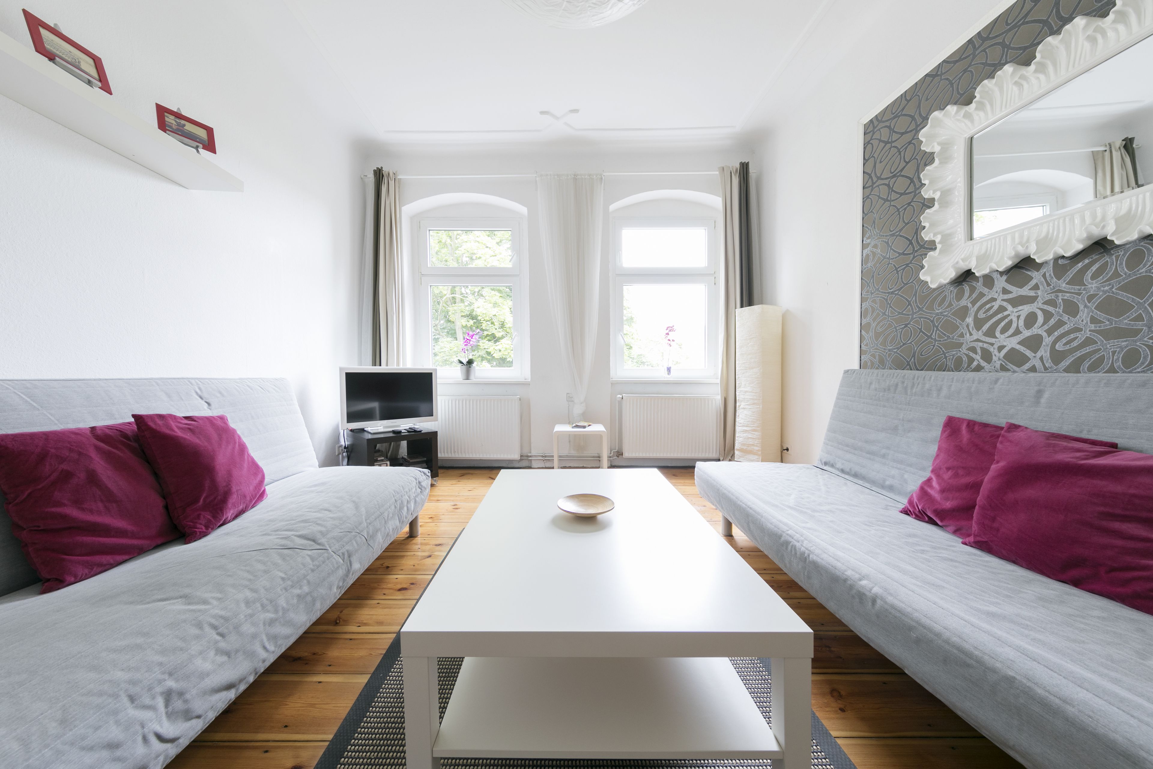 A modern living room with two grey sofas, a white coffee table, and a TV on a stand.