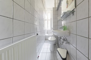 A modern bathroom with white tiles, a toilet, a sink, and a radiator.
