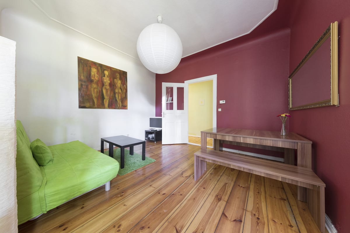 A living room with a green sofa, a wooden coffee table, a white lamp, and a painting on the wall.