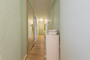 A narrow hallway with wooden flooring, a white refrigerator, and a door at the end.