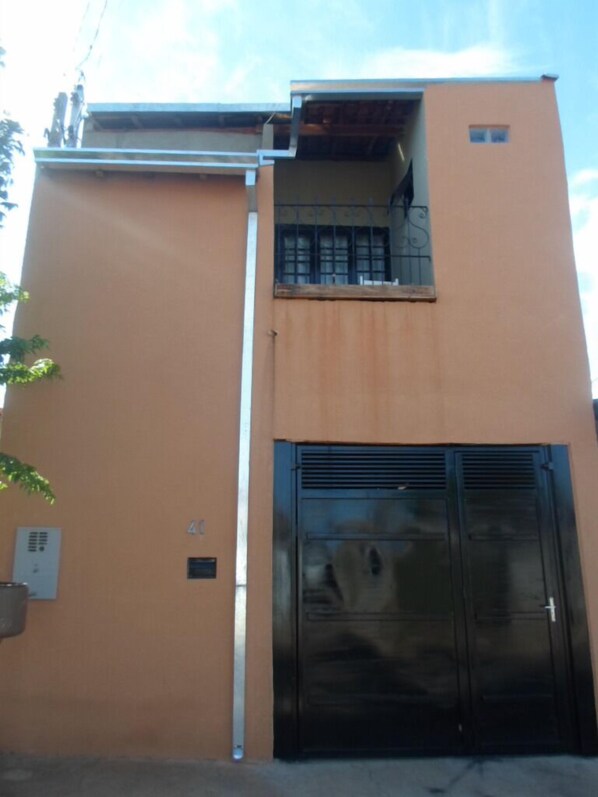 A building with a beige exterior, a black door, and a small balcony with metal railings.