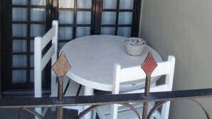 Un balcón con una mesa redonda y dos sillas, una puerta de vidrio esmerilado y una pequeña planta en maceta.