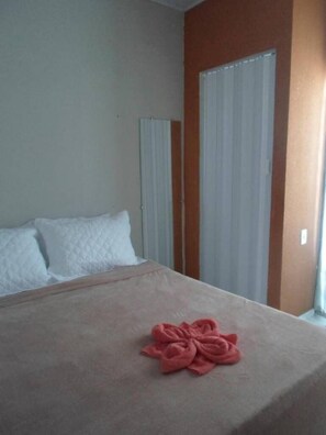A hotel room with a bed, white pillows, a red towel, and a window with blinds.
