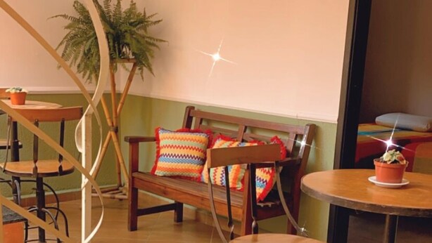 Una habitación acogedora con un banco de madera, sillas y una pequeña mesa con una planta en maceta. Hay un extintor en el suelo y una escalera con barandilla.