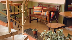 Un interior acogedor con una escalera de madera, una zona de estar con sillas y un banco, y una planta en maceta.