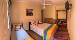 A hotel room with two single beds, a ceiling fan, a large window, a framed picture on the wall, and a wooden bench with a patterned cushion. - Pousada Ibituruna (São Paulo)