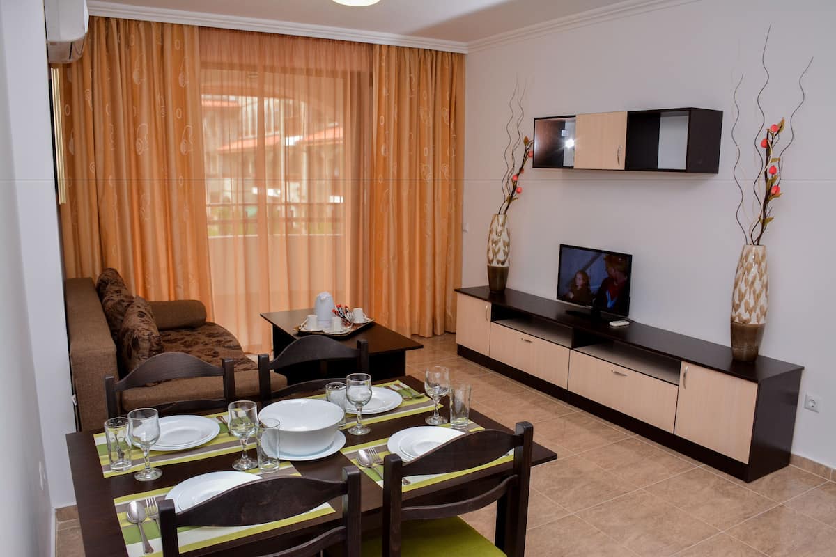 A dining area with a table set for four, a sofa, a TV, and decorative vases.