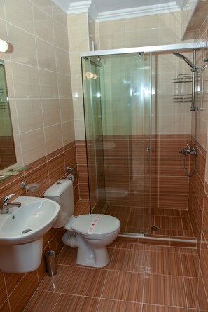 Un baño con ducha envuelta en vidrio, lavamanos e inodoro.