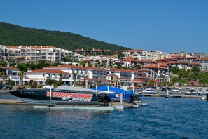 A marina with boats, including a speedboat with "VenisMarine Racing" written on it, and a backdrop of hillside buildings.