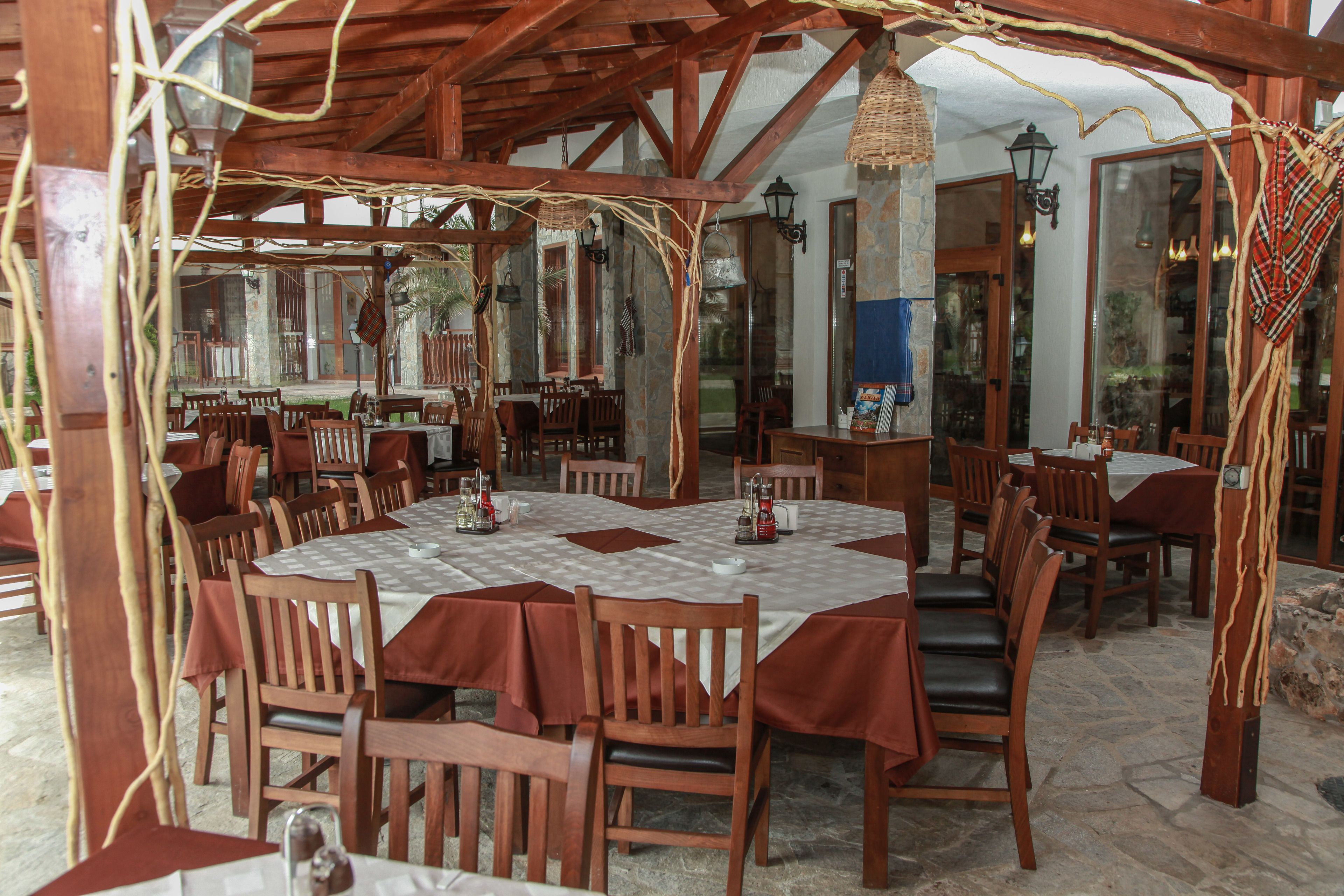 Un espace extérieur aménagé pour les repas, avec des tables et des chaises en bois, recouvertes de nappes blanches et de serviettes rouges.