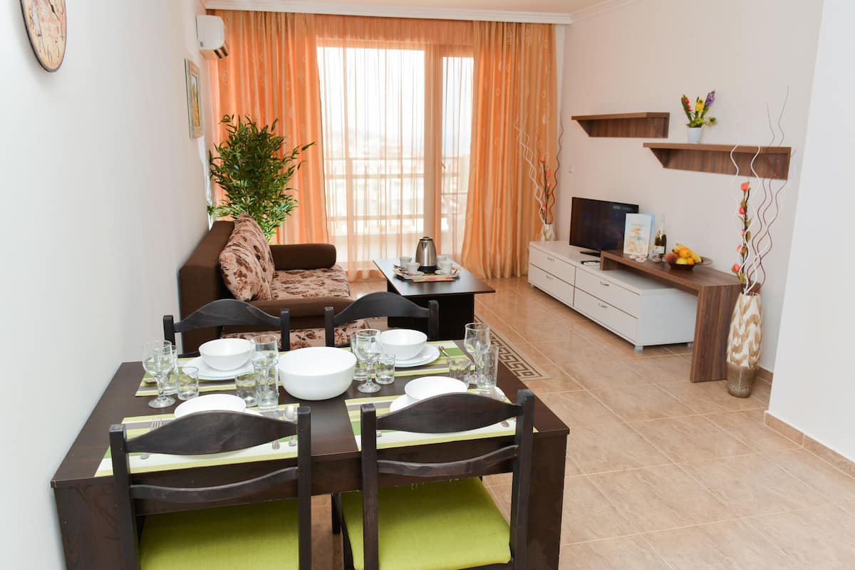 A dining area with a table set for four, a sofa, a TV, and a plant.