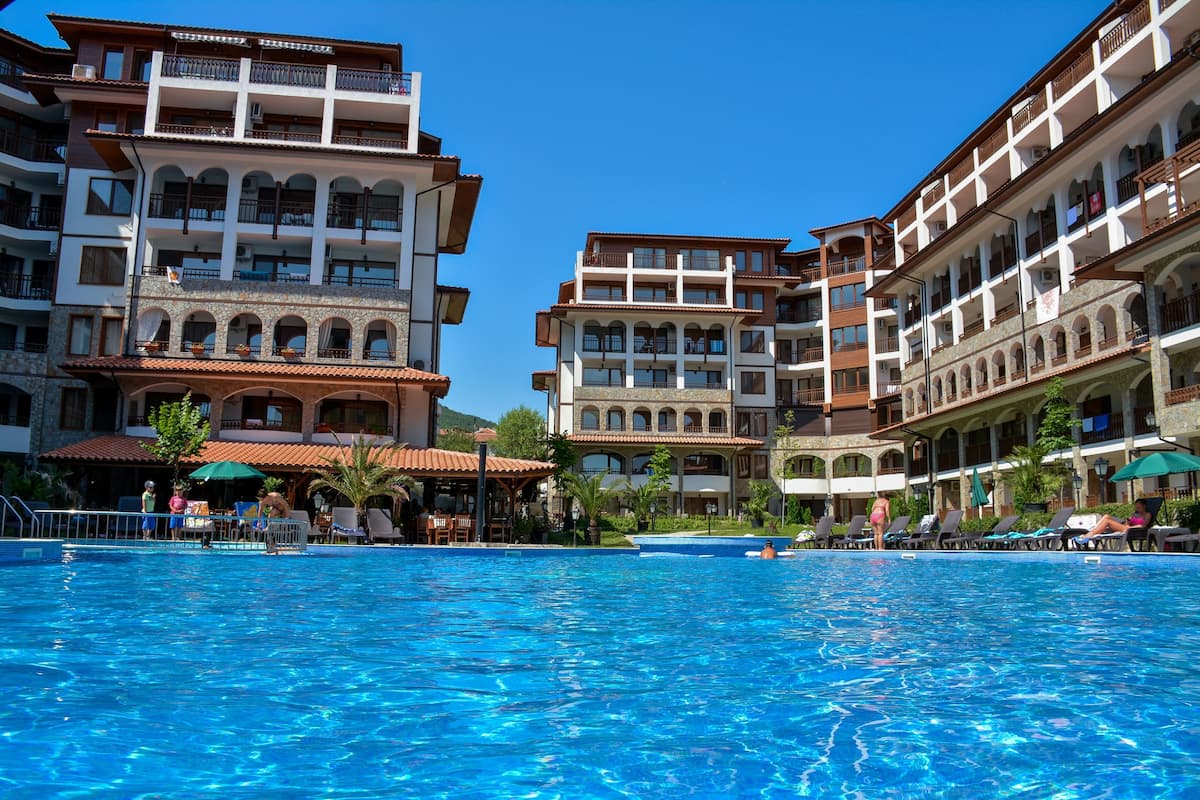 A hotel with multiple balconies, a swimming pool, and outdoor seating areas.