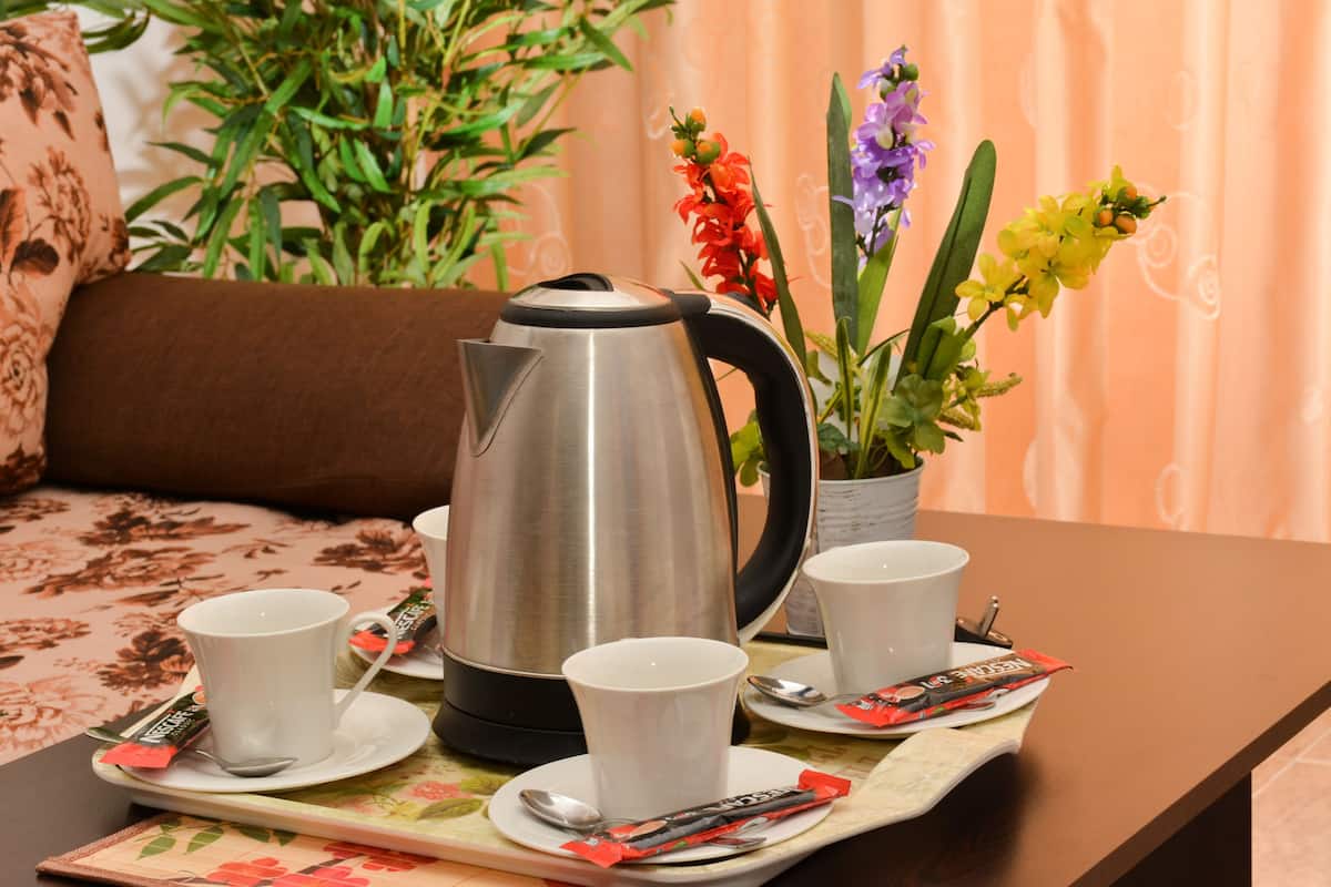 A table set with a stainless steel kettle, white cups, saucers, and a tray with packets and spoons.