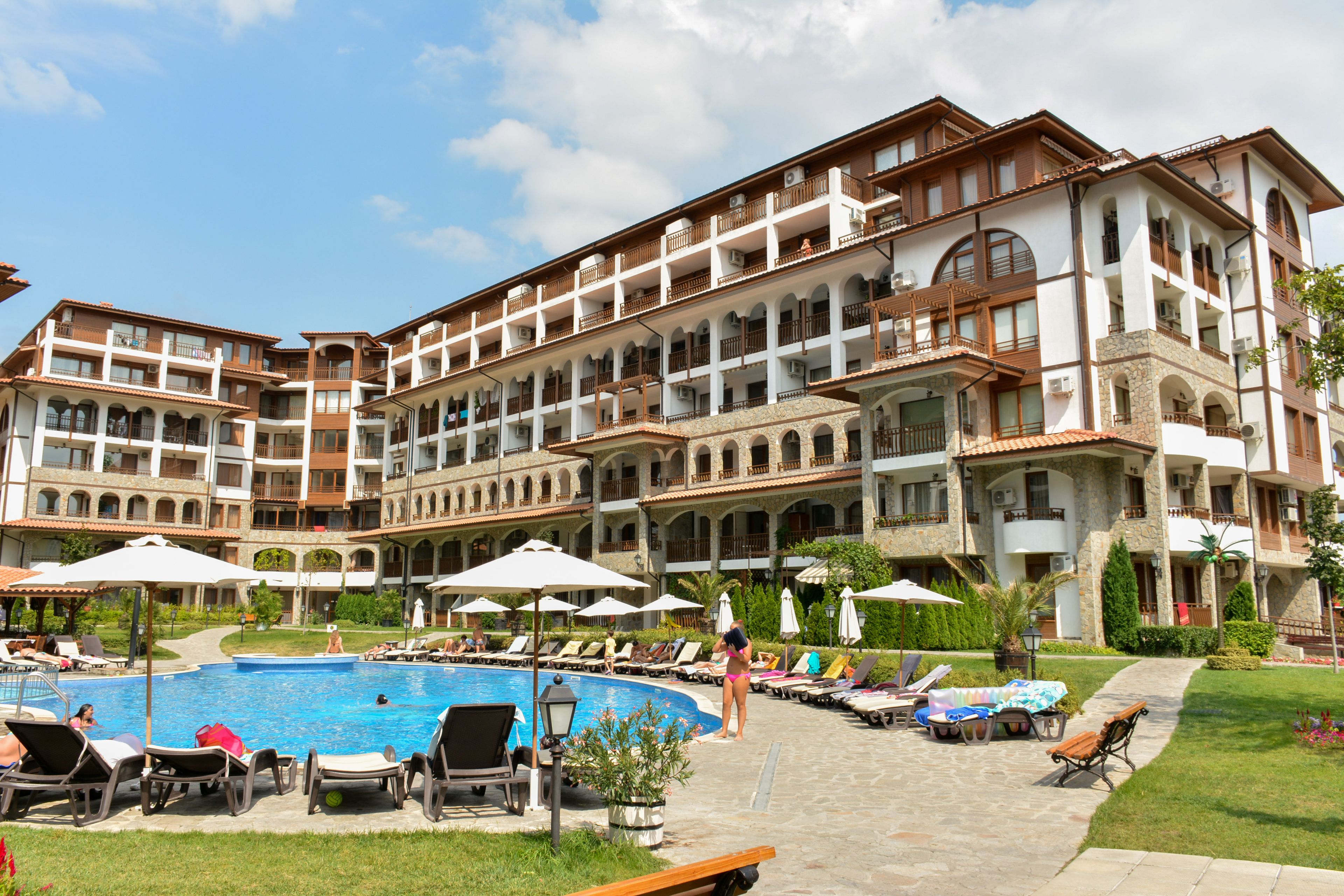A multi-story hotel with a swimming pool, outdoor seating, and a well-maintained garden.
