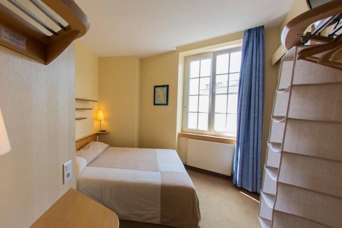 Una habitación de hotel con dos camas, una ventana con cortinas, una lámpara de noche y un radiador.
