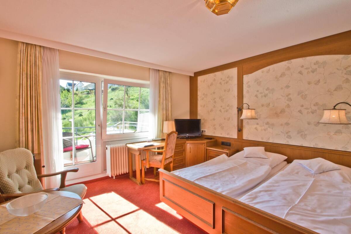 Une chambre d’hôtel équipée d’un lit, d’un bureau, d’une chaise, d’une télévision et d’une fenêtre avec des rideaux.