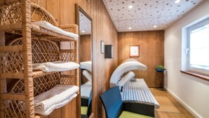A room with a wooden wall, a wicker shelf with towels, a massage chair, and a window. - Landgasthof Hotel Hanses-Bräutigam (Schmallenberg)