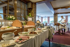 A buffet setup with various food items and a person serving in the background. - Landgasthof Hotel Hanses-Bräutigam (Schmallenberg)